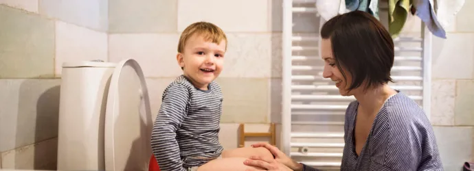 Un petit garçon souriant assis sur des toilettes accompagné de sa mère