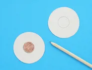 Deux cercles découpés dans du carton sont posés sur une surface bleue avec une pièce de monnaie au milieu d’un cercle et un crayon sur le côté