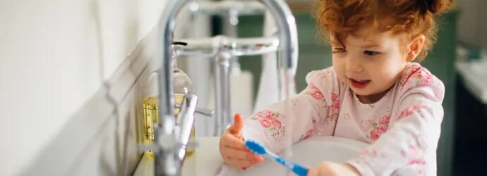 Une petite fille rousse lave sa brosse à dents dans un lavabo