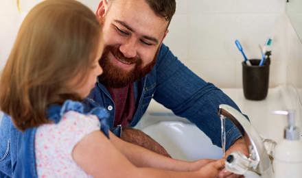 Isä auttaa tytärtään pesemään kädet juoksevan veden alla