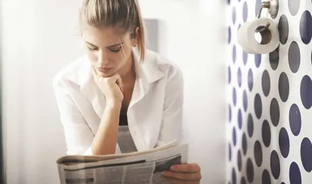 Une femme qui lit le journal aux toilettes