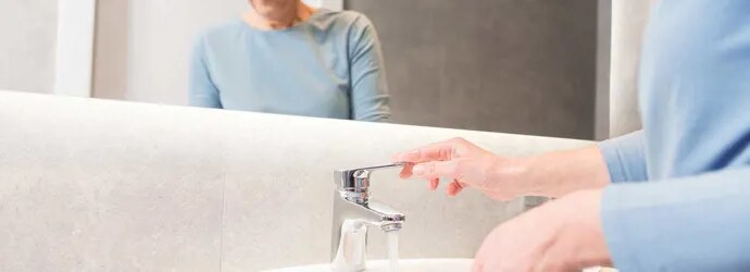 Une femme âgée utilise le robinet pour nettoyer sa brosse à dents