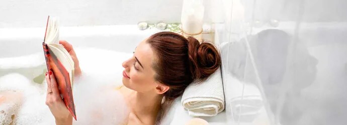 Une femme lit dans un bain à bulles avec des bougies allumées