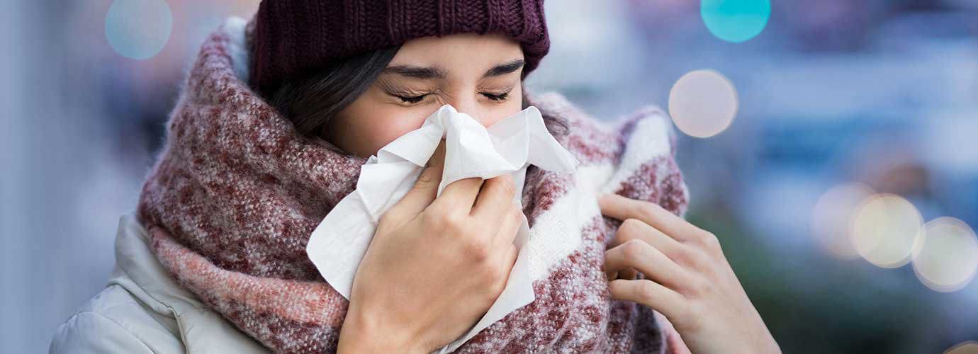 Paksuihin talvivaatteisiin sonnustautunut nainen kärsii poskiontelotulehduksen oireista ja aivastaa nenäliinaan ulkona