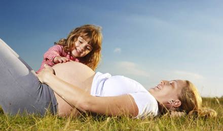 Une mère enceinte et son jeune enfant assis dans un champ avec un ciel bleu semble avoir besoin de soulager son rhume des foins pendant la grossesse.