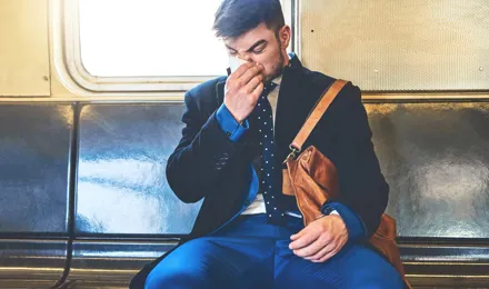 Un homme vêtu d'un costume se mouche assis dans un wagon de train