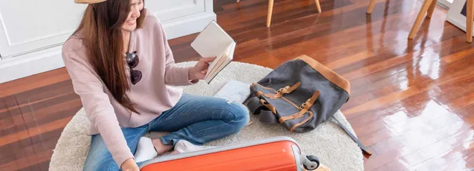 Une jeune femme assise sur le plancher prépare sa valise pour les vacances d'été
