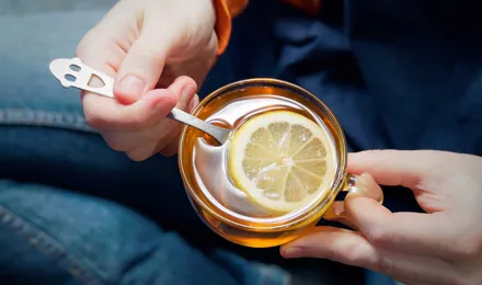 Une personne tient une tasse en verre remplie d'eau chaude avec du miel et du citron