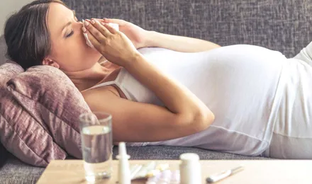 Une jeune femme enceinte avec un rhume sur le canapé.