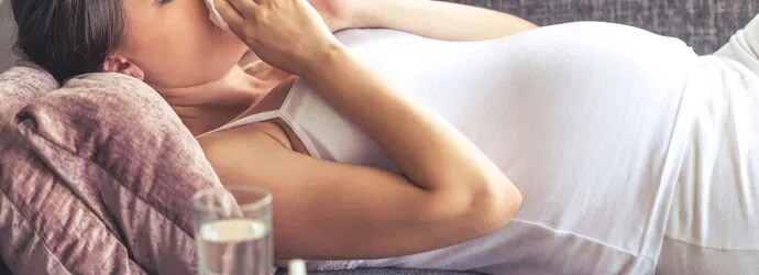 Une jeune femme enceinte avec un rhume sur le canapé.