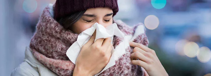 Femme enveloppée dans de gros vêtements d'hiver et qui souffre des symptômes de la sinusite,  elle éternue dans un mouchoir