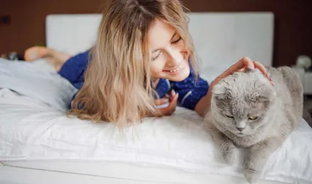 Nainen makaa sängyllä ja silittää kissaansa allergiaoireista kärsimättä