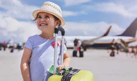 Une jeune fille souriante avec en arrière-plan une valise jaune avec des articles dont vous avez besoin pour des vacances en famille