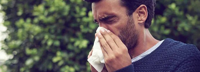 Un homme se mouche avec un mouchoir tout en ayant les yeux larmoyants et le nez qui coule