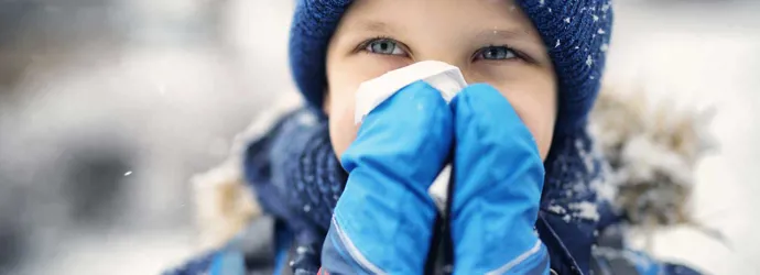 Un petit enfant vêtu de vêtements d'hiver se mouche le nez