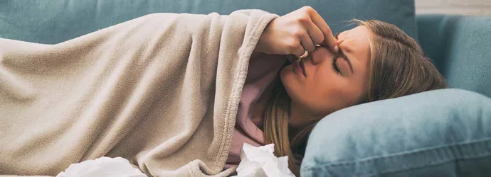 Une femme couchée dans un canapé bleu a des douleurs des sinus