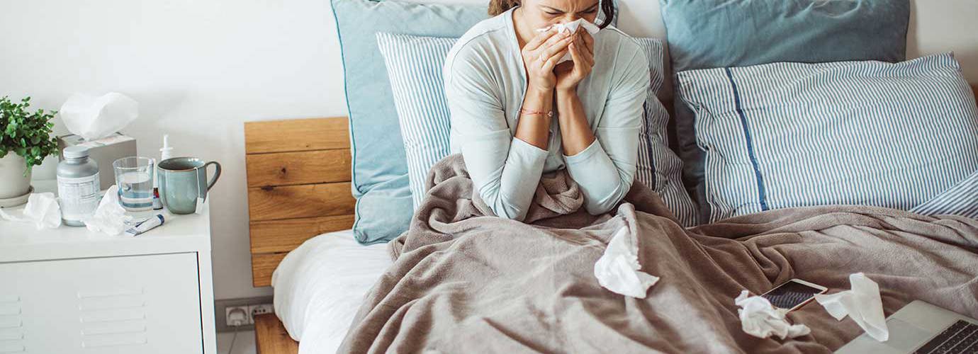 Une femme se mouche le nez dans son lit avec un mouchoir