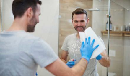 Sinisiin suojakäsineisiin sonnustautunut nainen puhdistaa kylpyhuoneen peiliä