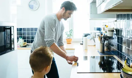 Mies puhdistaa keittiötasoa lapsen katsoessa tarkasti vierestä