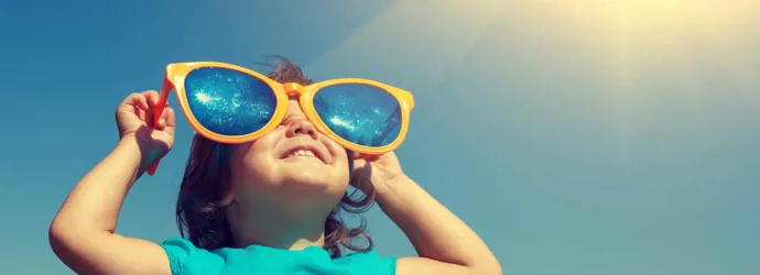 Un jeune enfant avec une paire de lunettes de soleil surdimensionnées et comiques fait le plein de vitamine D grâce au soleil dans le ciel