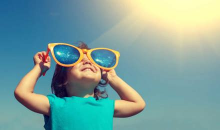Un jeune enfant avec une paire de lunettes de soleil surdimensionnées et comiques fait le plein de vitamine D grâce au soleil dans le ciel