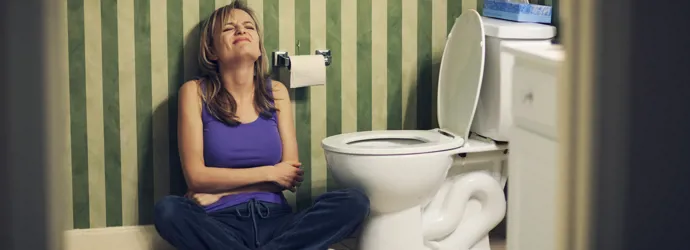 Femme assise par terre à côté des toilettes, se tenant le ventre de douleur
