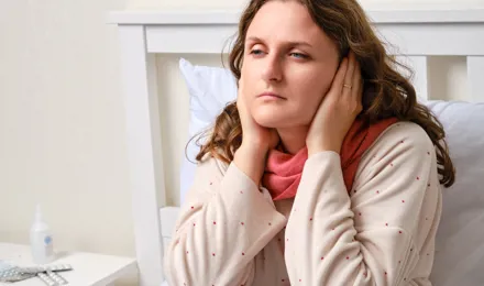 Femme malade assise sur un lit, ayant ses mains sur ses oreilles