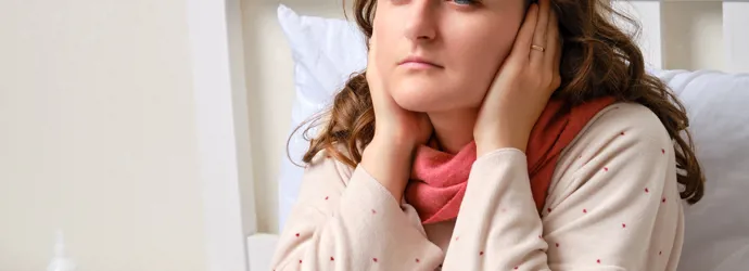Femme malade assise sur un lit, ayant ses mains sur ses oreilles