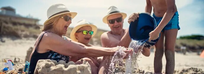 Deux enfants et leurs grands-parents à la plage, construisant un château de sable