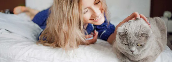 Une femme allongée sur son lit, caresse son chat, elle ne présente pas clairement les symptômes d'allergie aux poils de chat